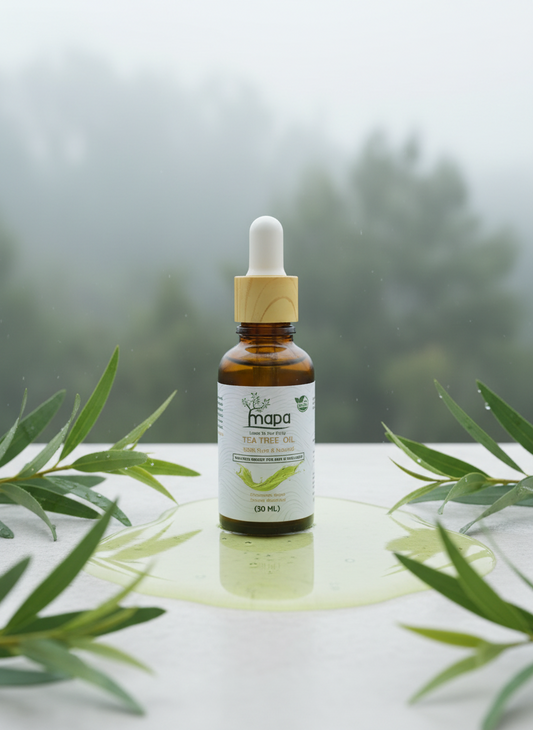 Bottle of mapa tea tree oil with dropper on a white surface with green leaves.